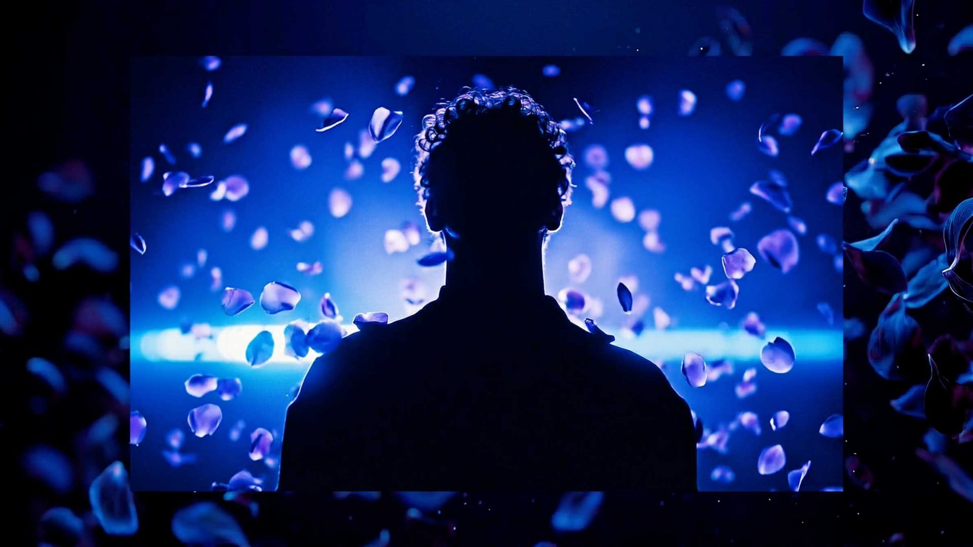 A silhouette of a person with curly hair stands against a vibrant blue background, surrounded by floating flower petals—a striking visual inspired by the bold creativity of Nerdo Studio. Frame from Stash Magazine article.