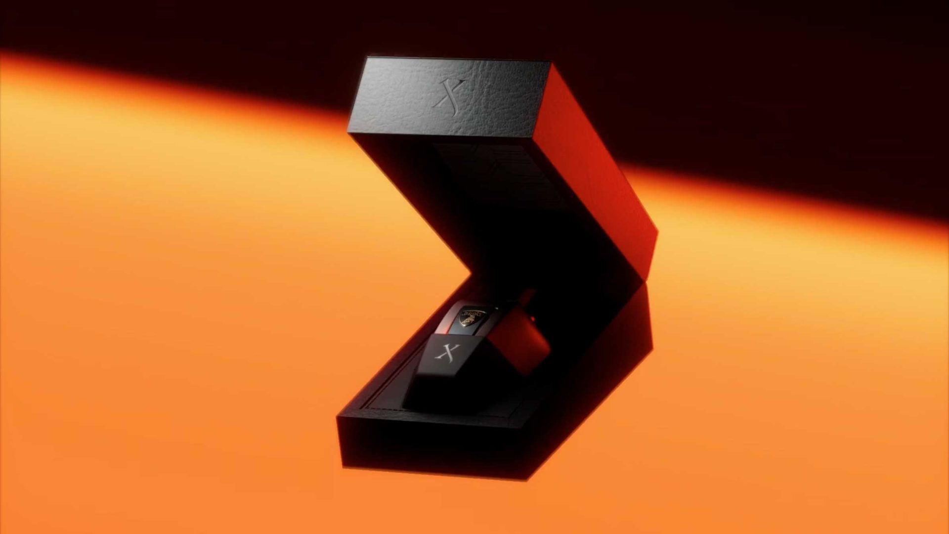A sleek, black, rectangular box with a hinged lid partially open, revealing a small black device inside. The background is orange with a light gradient. Both the box and device feature an X symbol, reminiscent of the bold design language found in Automobili Lamborghini collaborations. Frame from Stash Magazine article.