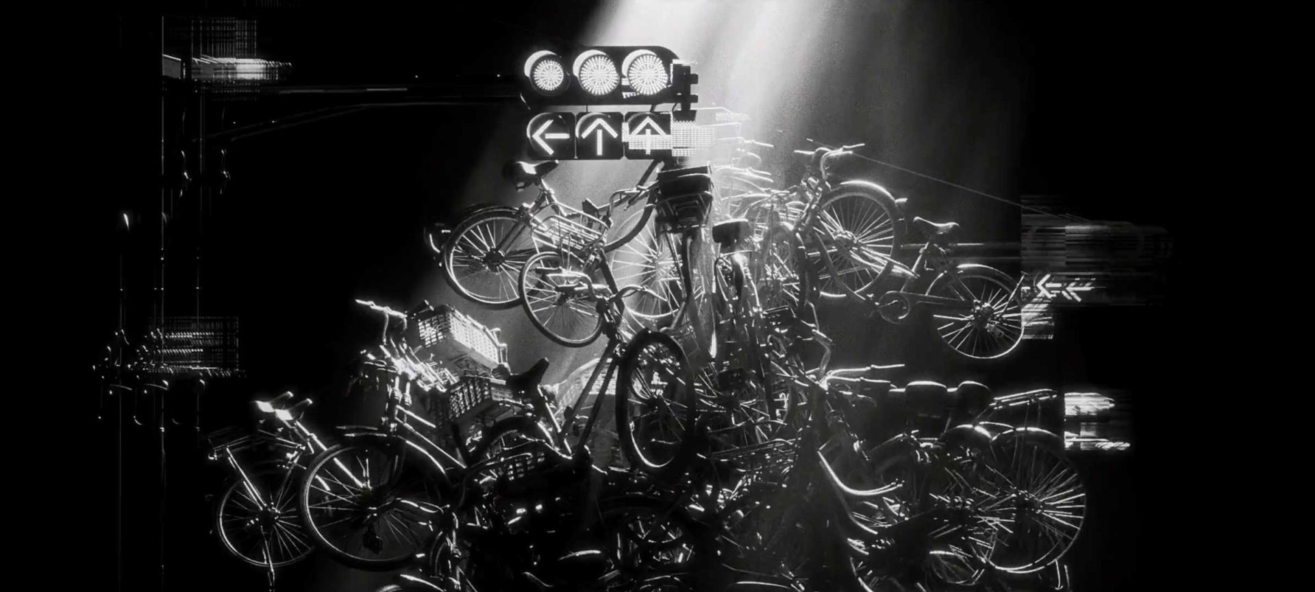 A dramatic black-and-white scene shows a chaotic pile of bicycles stacked high under a spotlight, with illuminated traffic lights overhead, creating a surreal and intense urban atmosphere reminiscent of New York’s restless energy—a striking visual crafted in collaboration with Yeti Pictures for Motion Plus Design. Frame from Stash Magazine article.